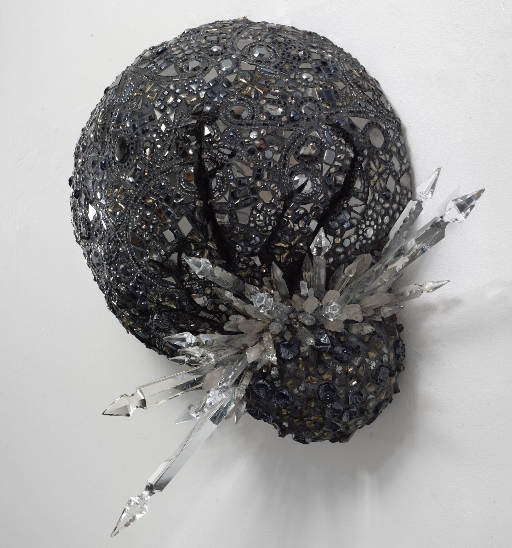 a round sculpture covered in a glimmering black mosaic with sharp clear crystals jutting out near the bottom right along with another bulbous shape