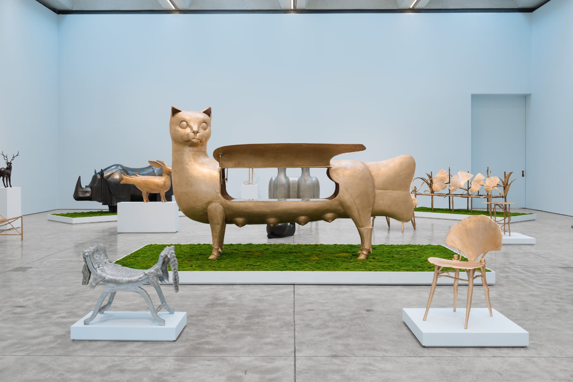 an installation view with a cat sculpture that opens up on its back surrounded by additional chair sculptures