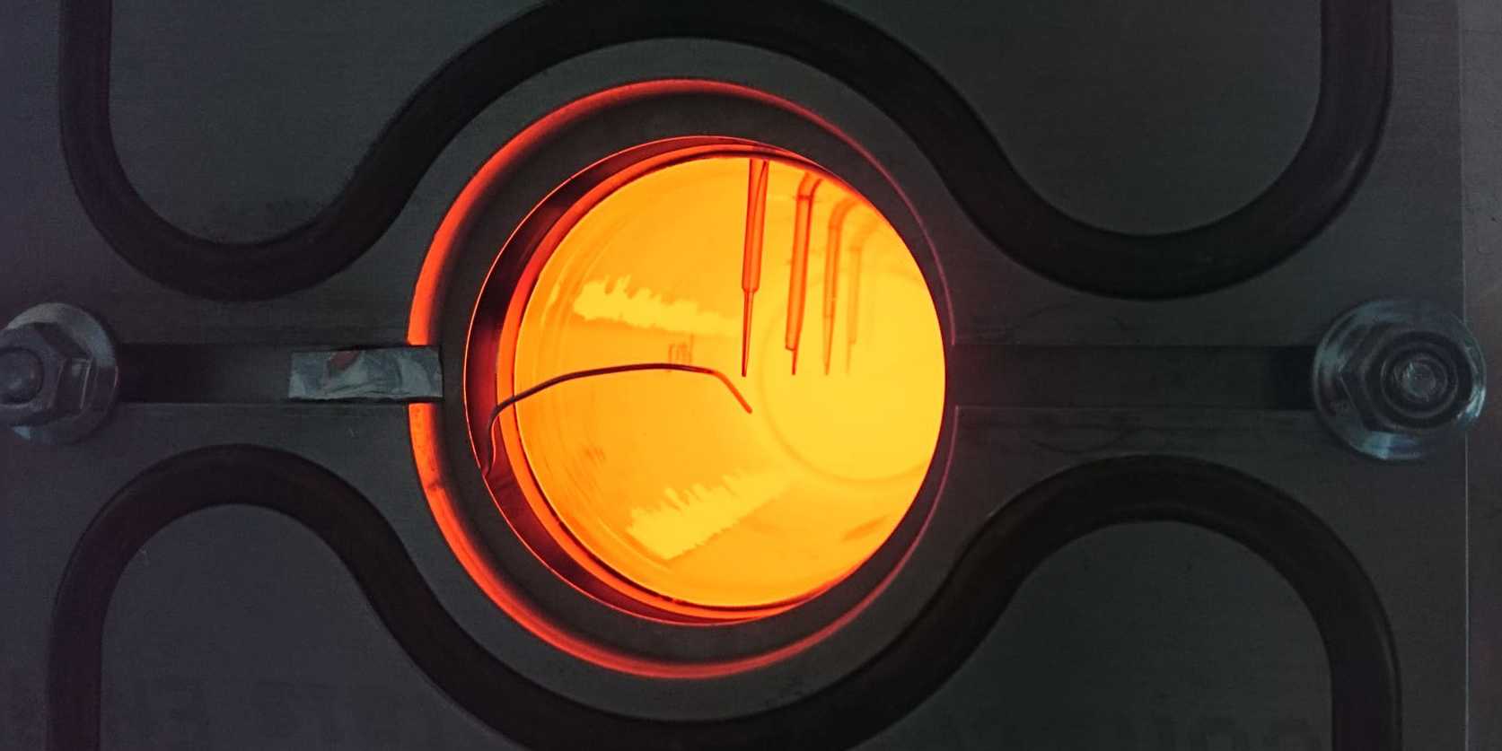 An image of an orange, translucent glowing quartz rod. Thermocouples can be seen at intervals along the rod looking in.