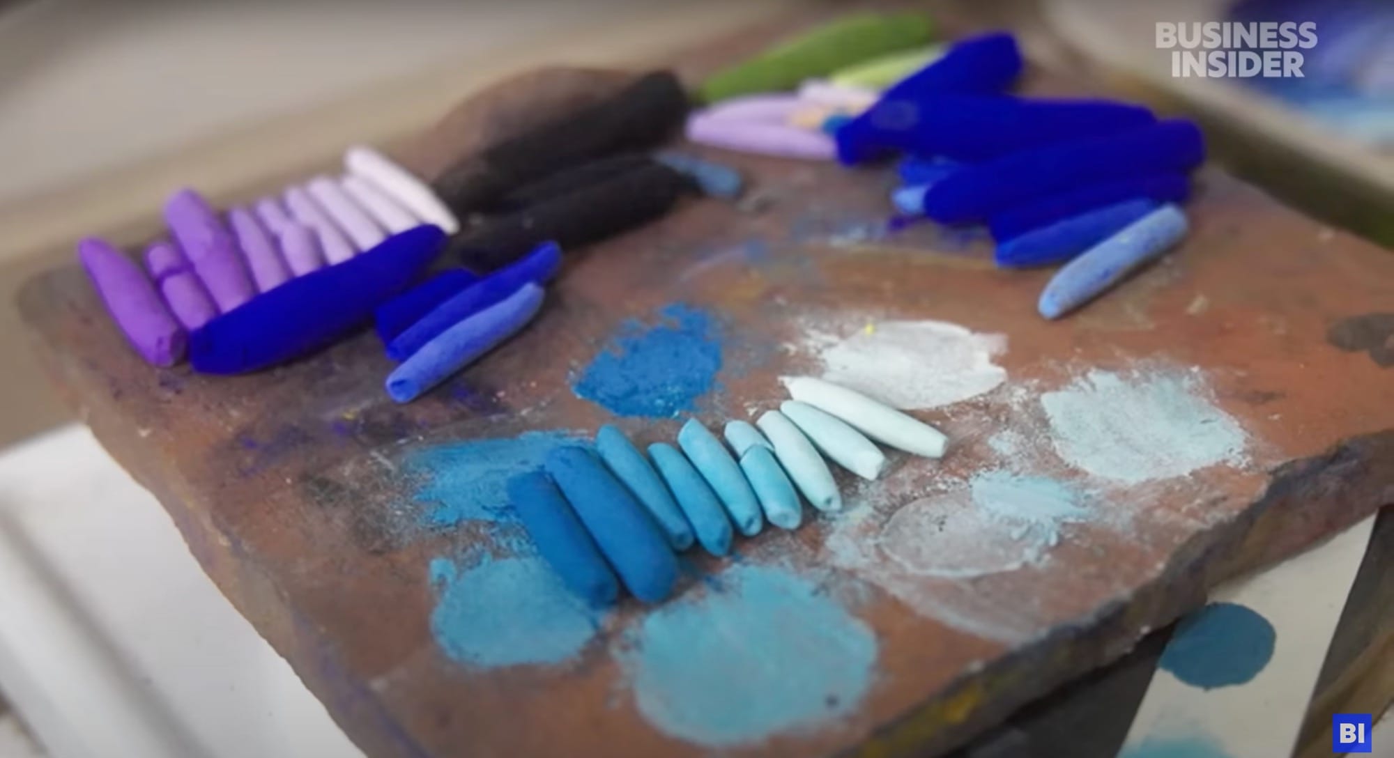 a still from a short documentary about a pastel maker in France, showing a table of numerous hand-rolled pigmented pastels with some test spots on a tray