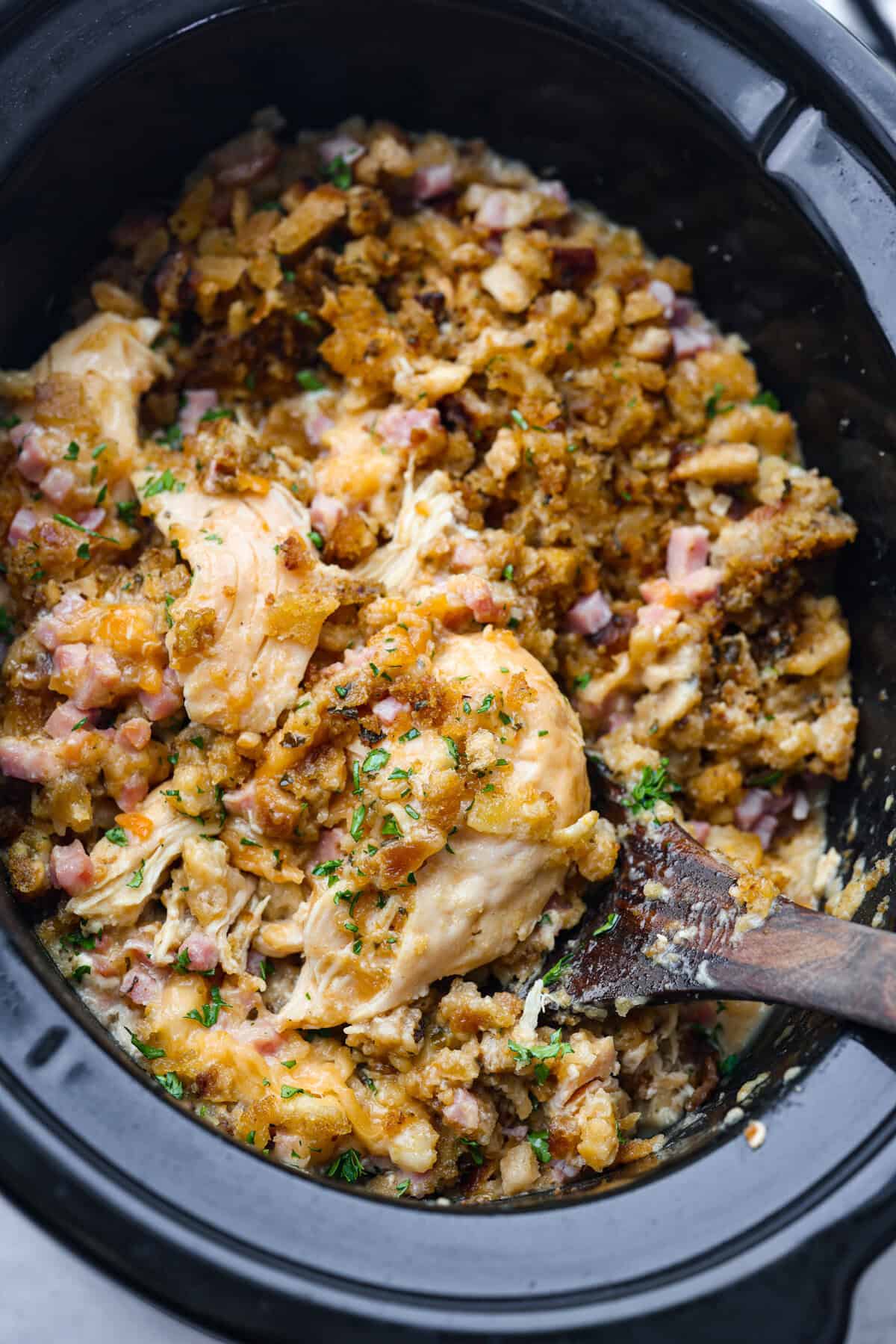 Slow cooker chicken cordon bleu in the crockpot being scooped out with a wooden spoon.