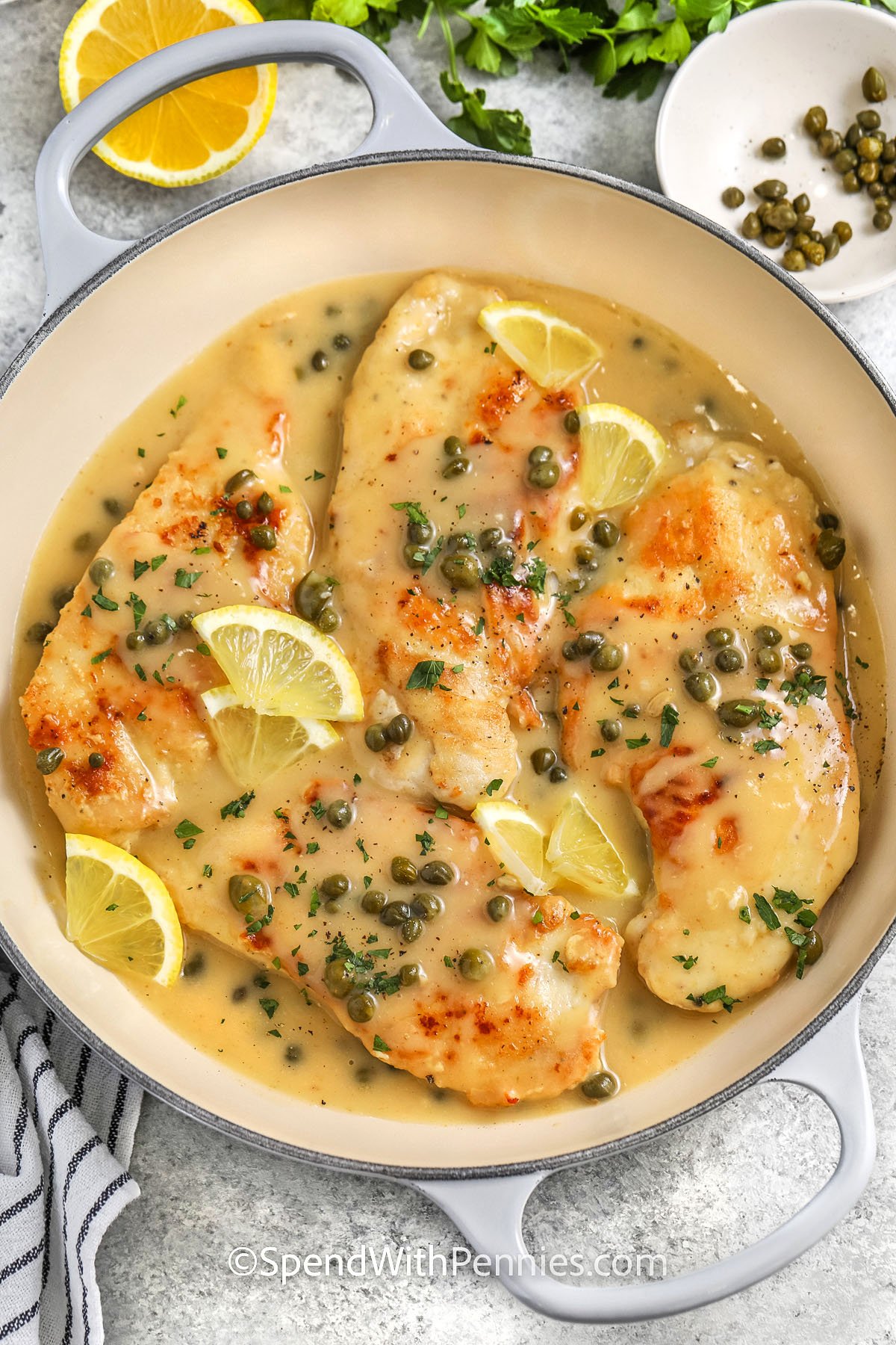 a skillet of chicken piccata with lemon slices and capers