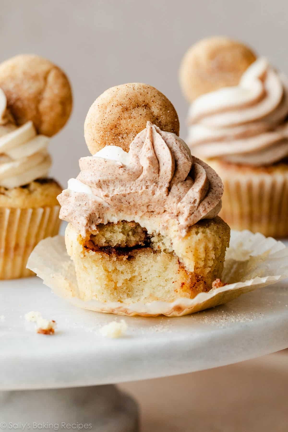 snickerdoodle cinnamon-swirled cupcake with bite taken out on marble cake stand.