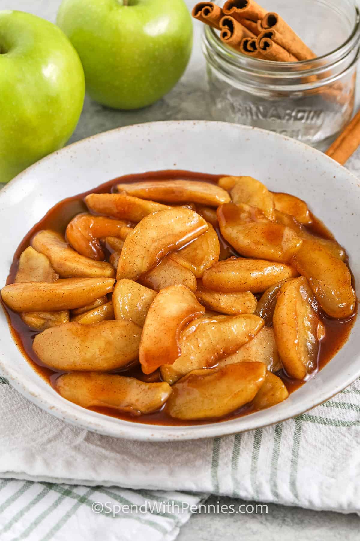 fried apples in a bowl with cinnamon sticks and apples in the background